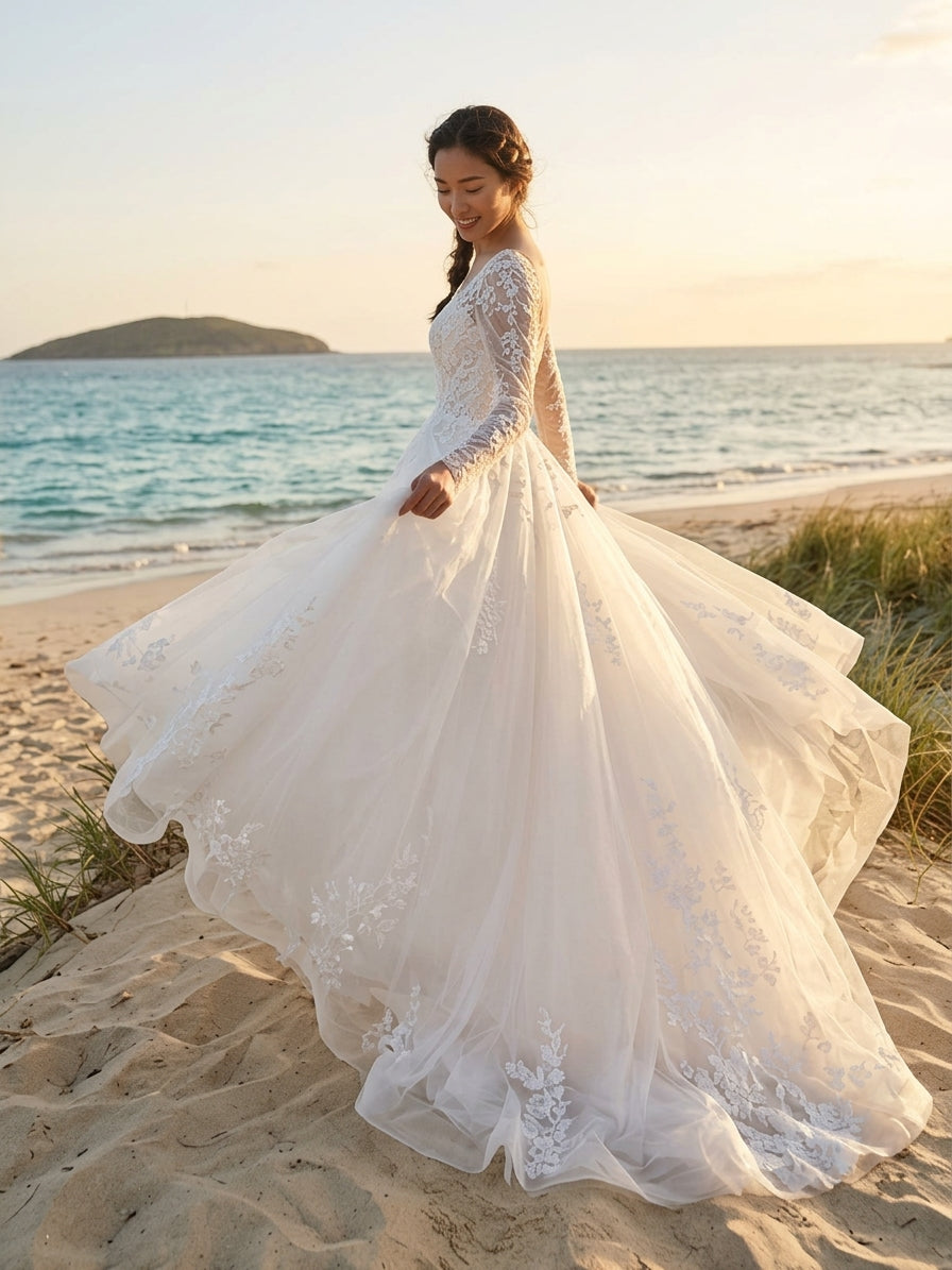 Lacey Bridal Ltd. Clementine A-line wedding gown with floral lace sleeves and tulle skirt on a sunny beach.