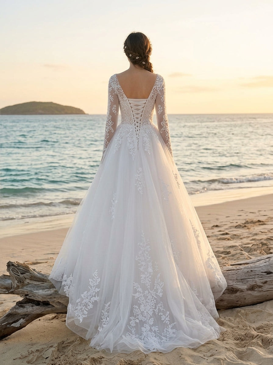 Lacey Bridal Ltd. Clementine A-line wedding gown with long illusion sleeves, lace appliqué, and corset back on a beach.