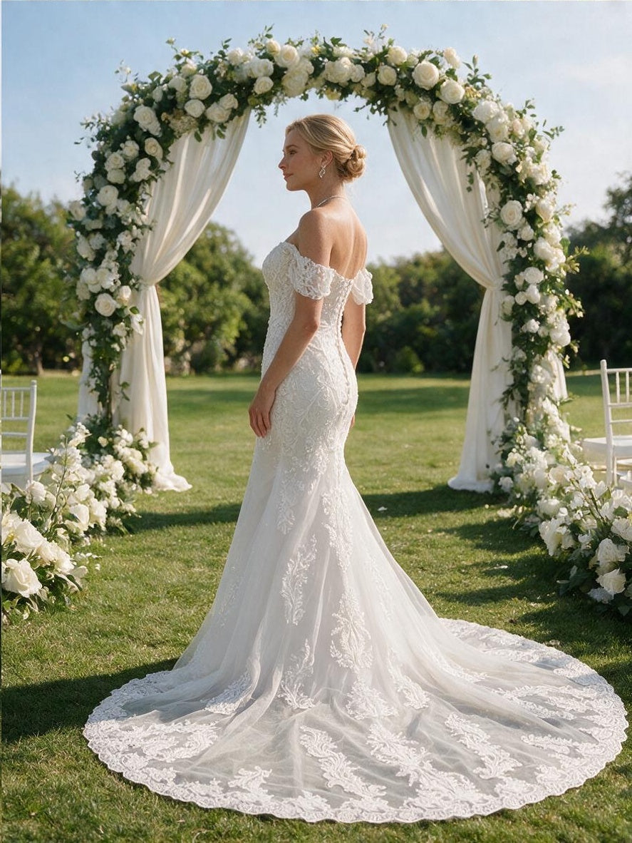 Lacey Bridal Ltd. GLORIA off-the-shoulder mermaid wedding gown with lace bodice and sheer train in a garden setting