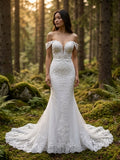 Lacey Bridal Ltd. Leona mermaid wedding gown with off-the-shoulder lace straps and botanical embroidery in a forest.