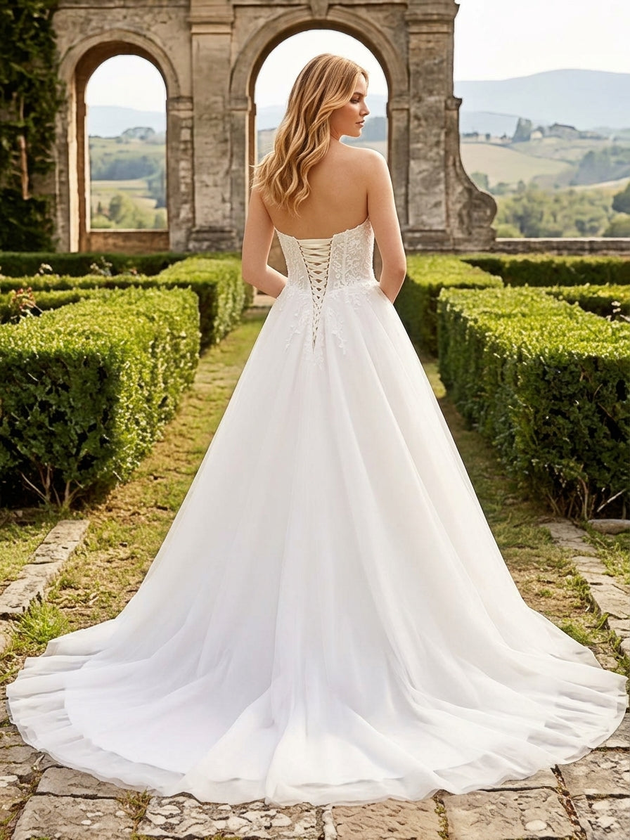 Lacey Bridal Ltd. Natalia strapless A-line wedding gown with lace-up corset back and flowing tulle skirt in a garden.