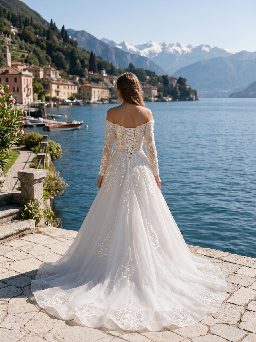 Lacey Bridal Ltd. OTTAVIA off-the-shoulder A-line wedding gown with lace sleeves and corset back by a scenic lake.