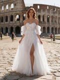 Lacey Bridal Ltd. Primrose A-line wedding gown with 3D floral lace, puff sleeves, and a high slit in front of Colosseum