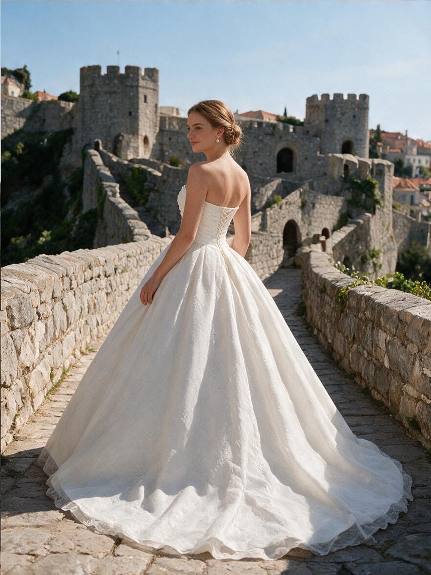 Lacey Bridal Ltd. Sabina strapless ballgown with a corset back and textured jacquard skirt on a stone castle bridge.