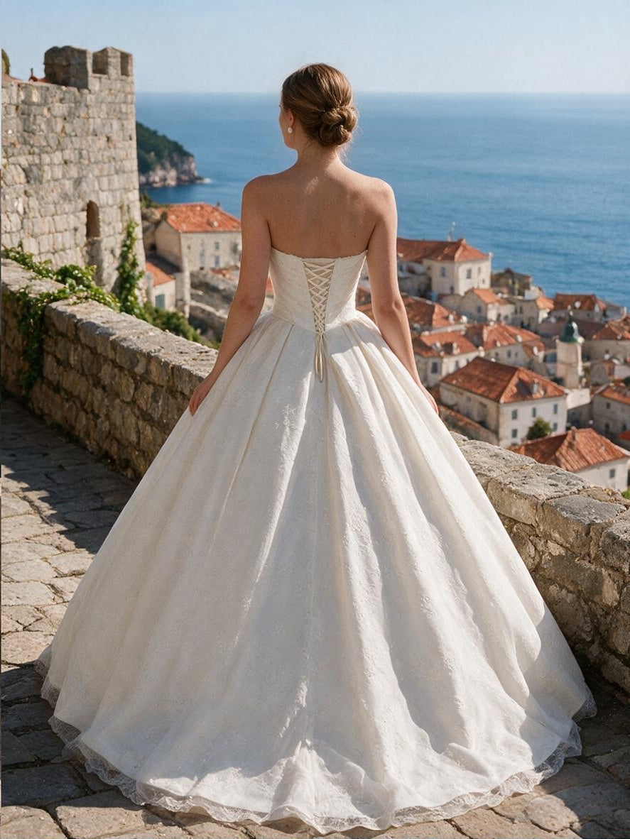 Lacey Bridal Ltd. SABINA strapless ballgown with a corset back and textured jacquard fabric overlooking the sea.