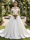 Lacey Bridal Ltd. Sophia satin ball gown with off-the-shoulder neckline and A-line skirt in a garden setting.