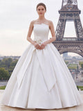 Lacey Bridal Ltd. strapless white satin ballgown with architectural folded neckline and floral waist accent in Paris.
