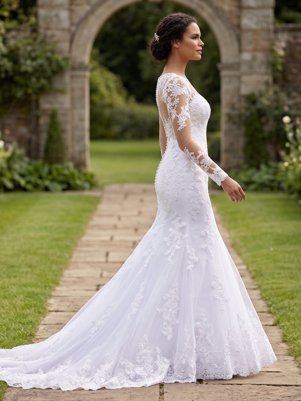 Lacey Bridal Ltd. THESPIA mermaid wedding gown with long illusion lace sleeves and a sweeping tulle train in a garden.