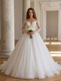 Lacey Bridal Ltd. Zelina ball gown with illusion long sleeves, lace appliqué, and a full tulle skirt in a ballroom.
